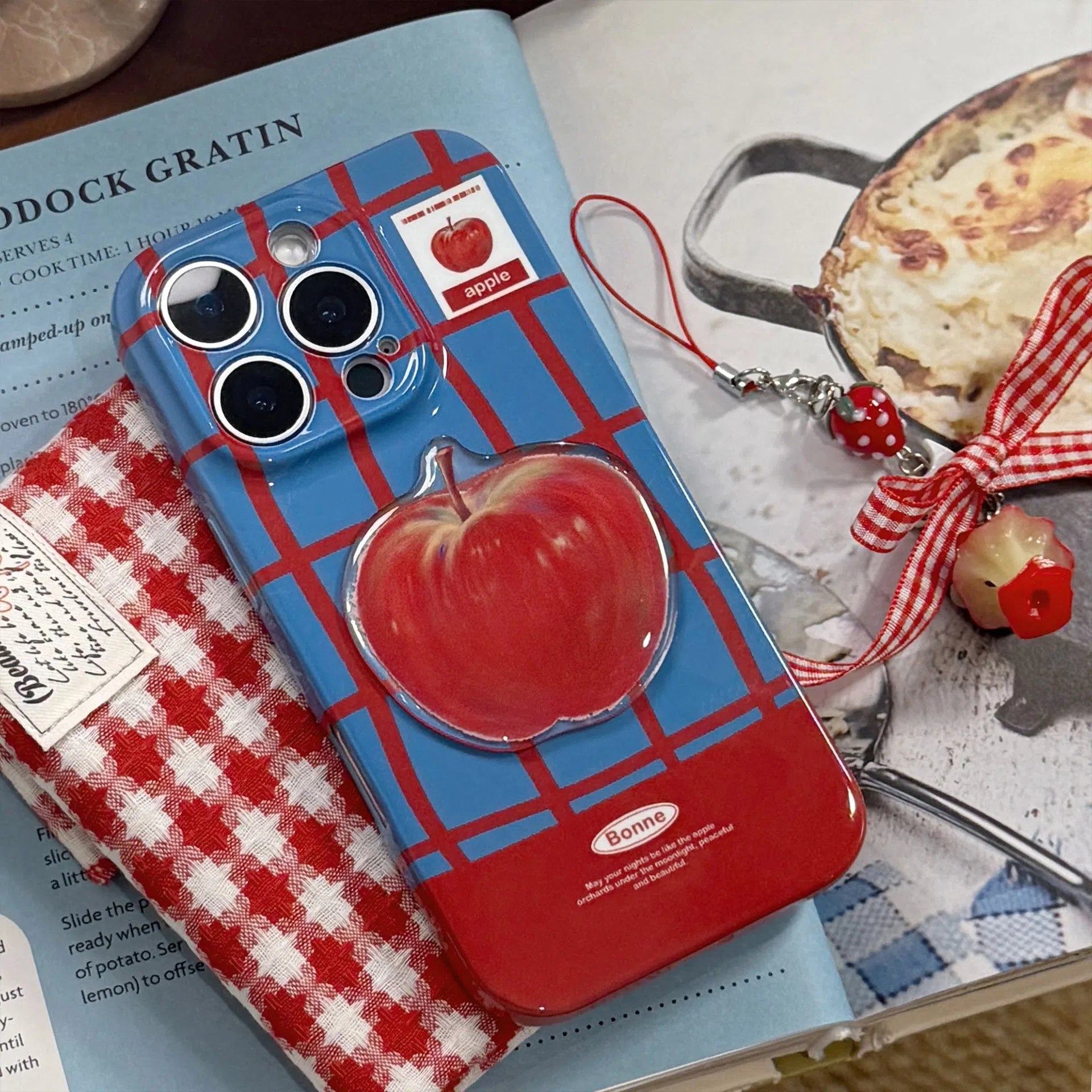 Colour-block checkered 3D fruit phone case for iPhone with blue red grid pattern and red fruit design pendant on a white background