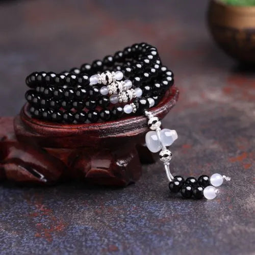 Natural black and red agate 108 bead bracelet with geometric shapes on a wrist.