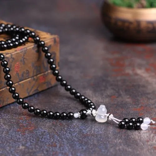 Natural black and red agate 108 bead bracelet with geometric shapes on a wrist.