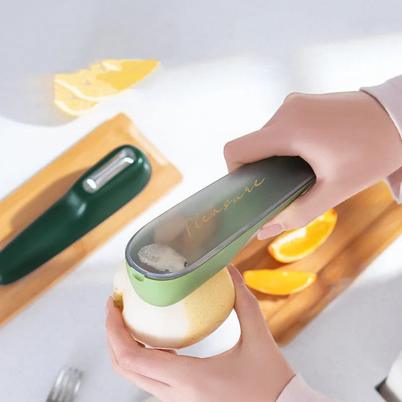 Dark green kitchen peeler with a storage tube, stainless steel blade, and non-slip plastic handle on a worktop.