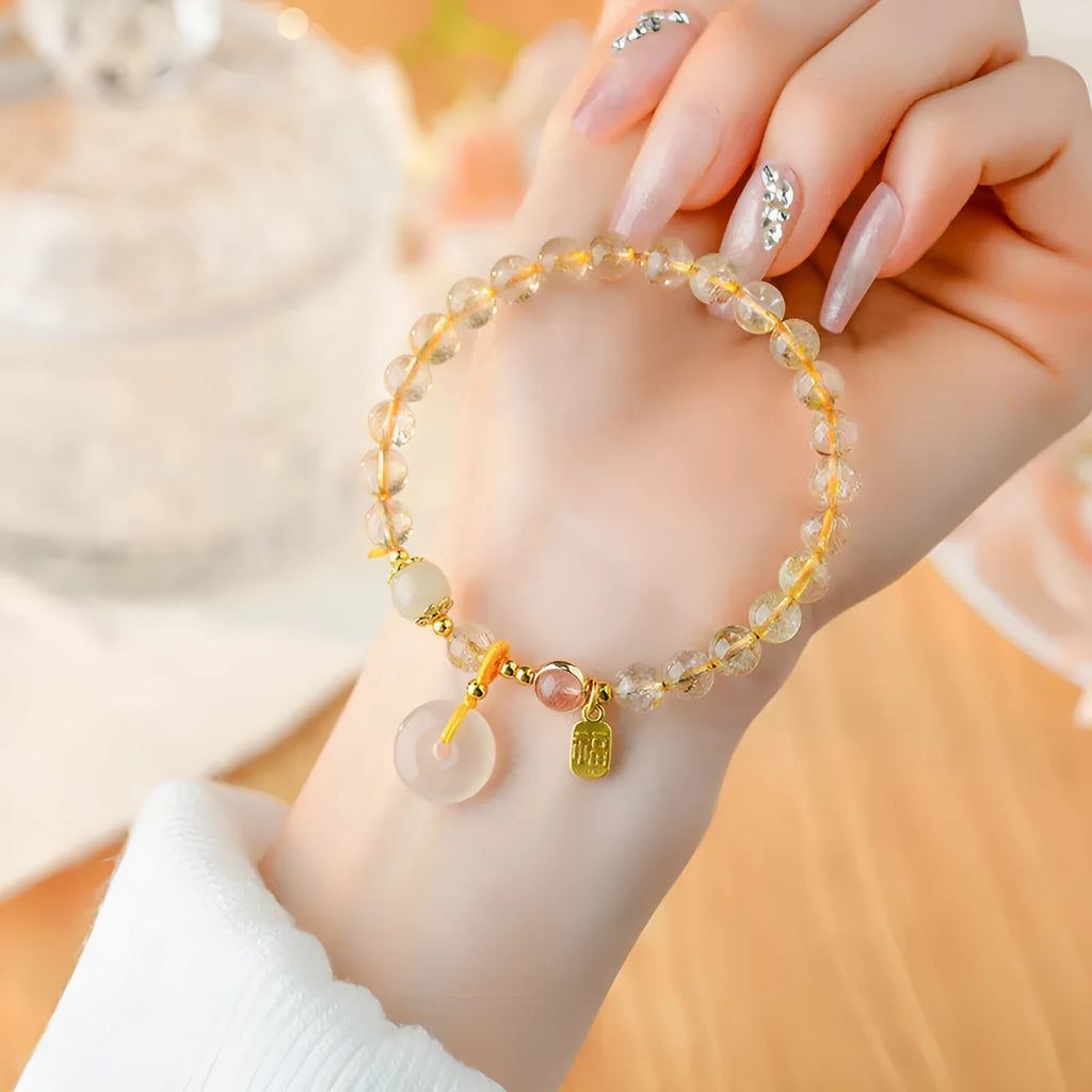 Gold rutilated quartz bracelet with geometric safety buckle and pendant on a white background.