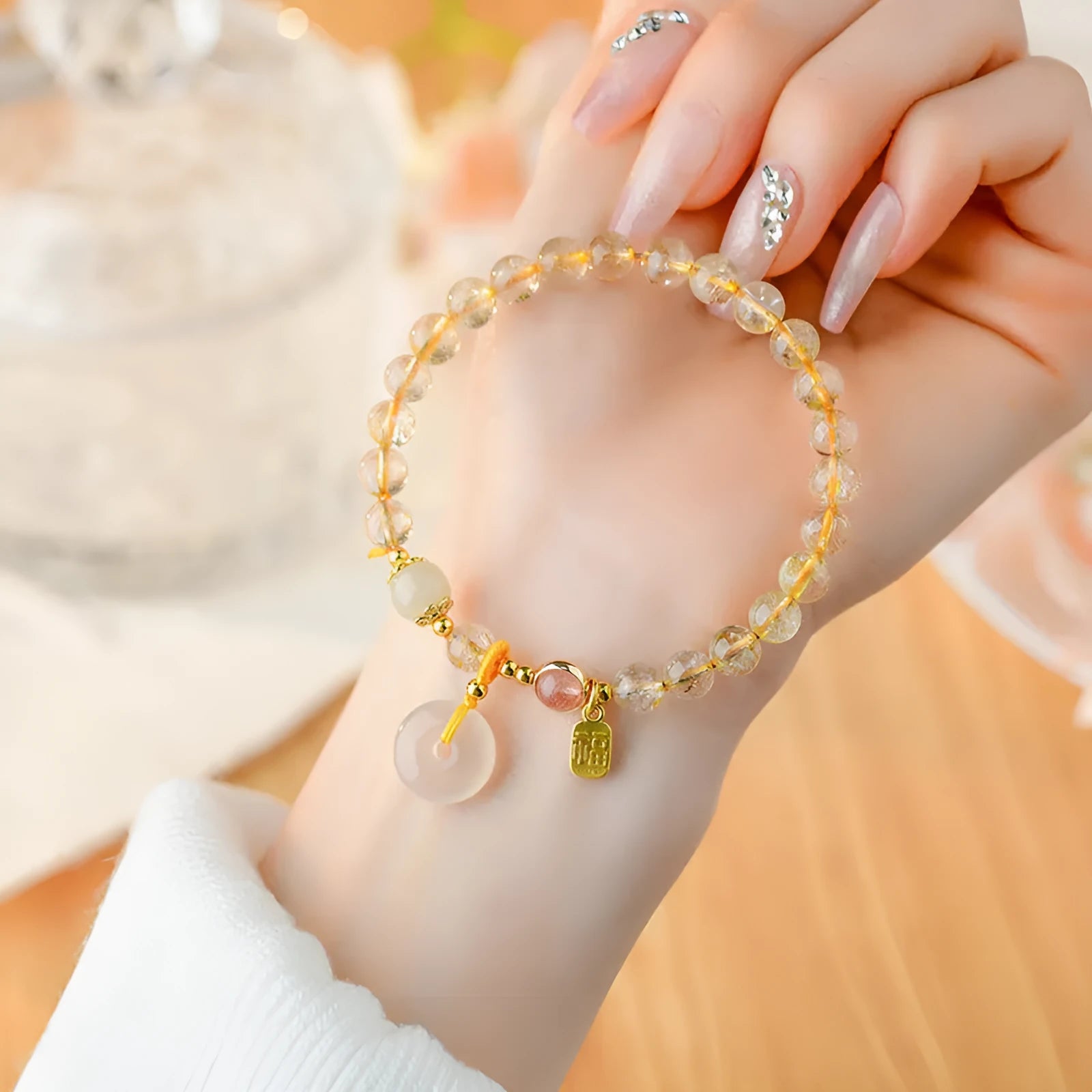 Gold rutilated quartz bracelet with geometric safety buckle and pendant on a white background.