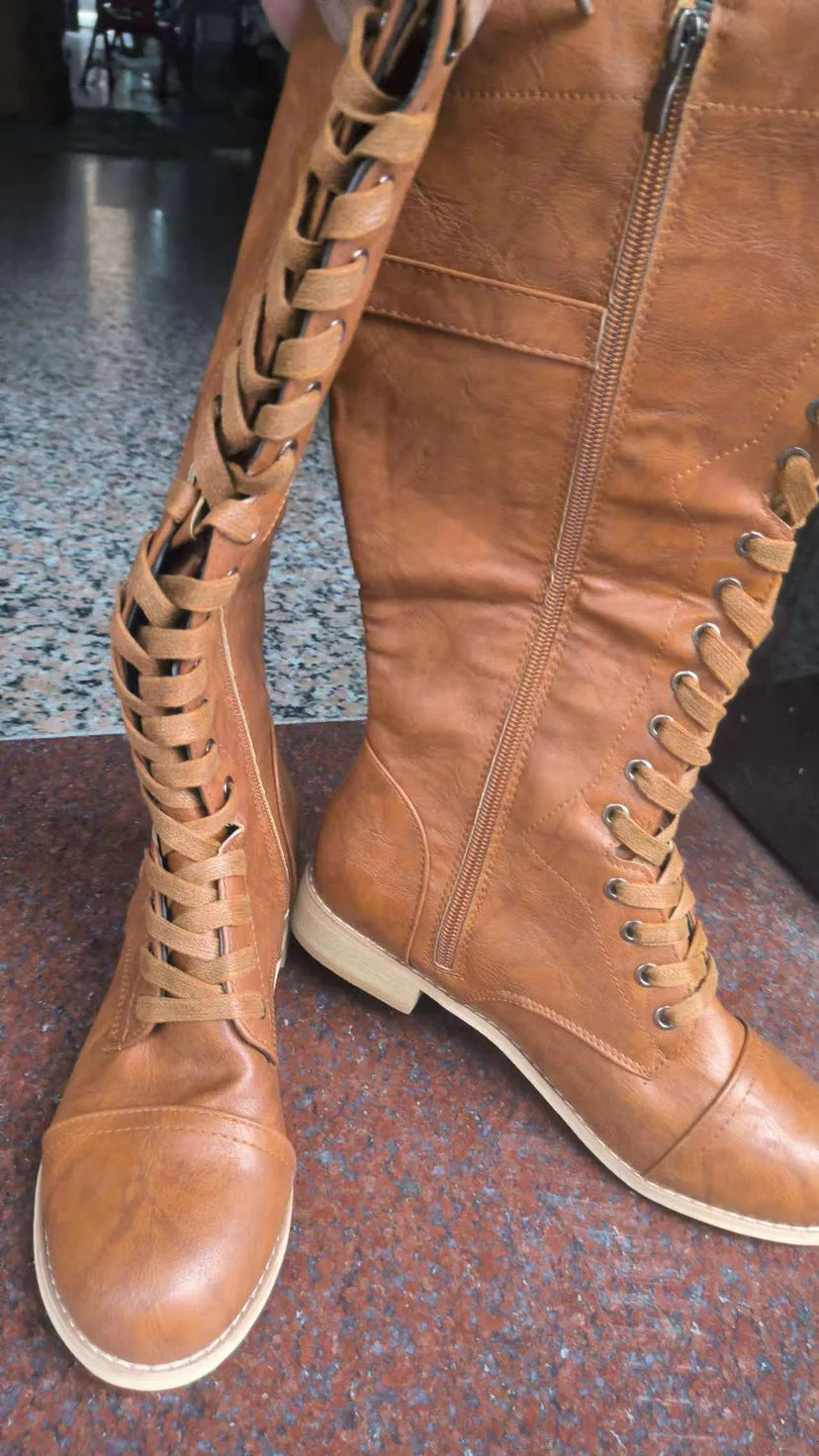 Women's black knee-high boots with a cross-strap buckle and elastic back panel.