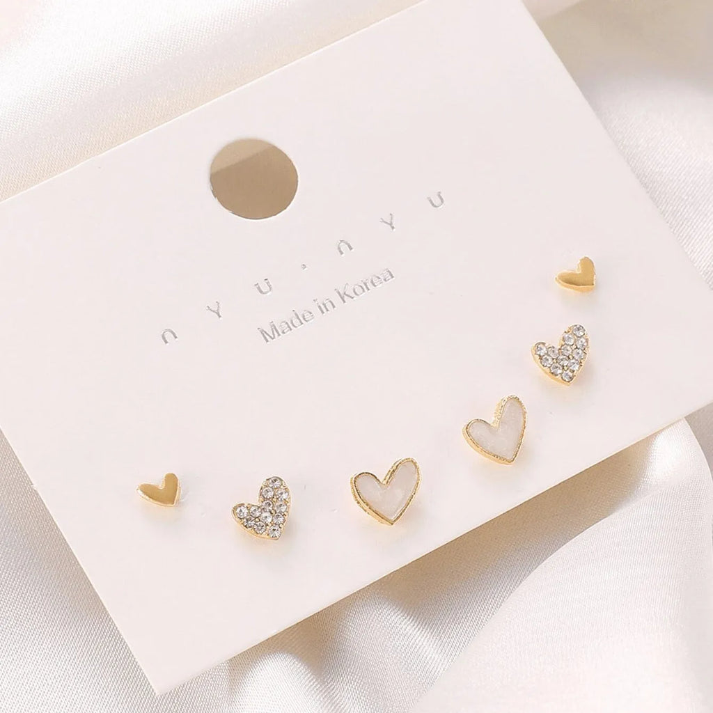 Three pairs of women's heart-shaped earrings in gold, black, black and white, and pink colours