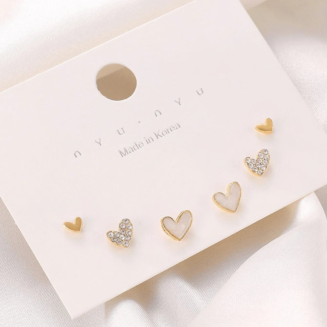 Three pairs of women's heart-shaped earrings in gold, black, black and white, and pink colours