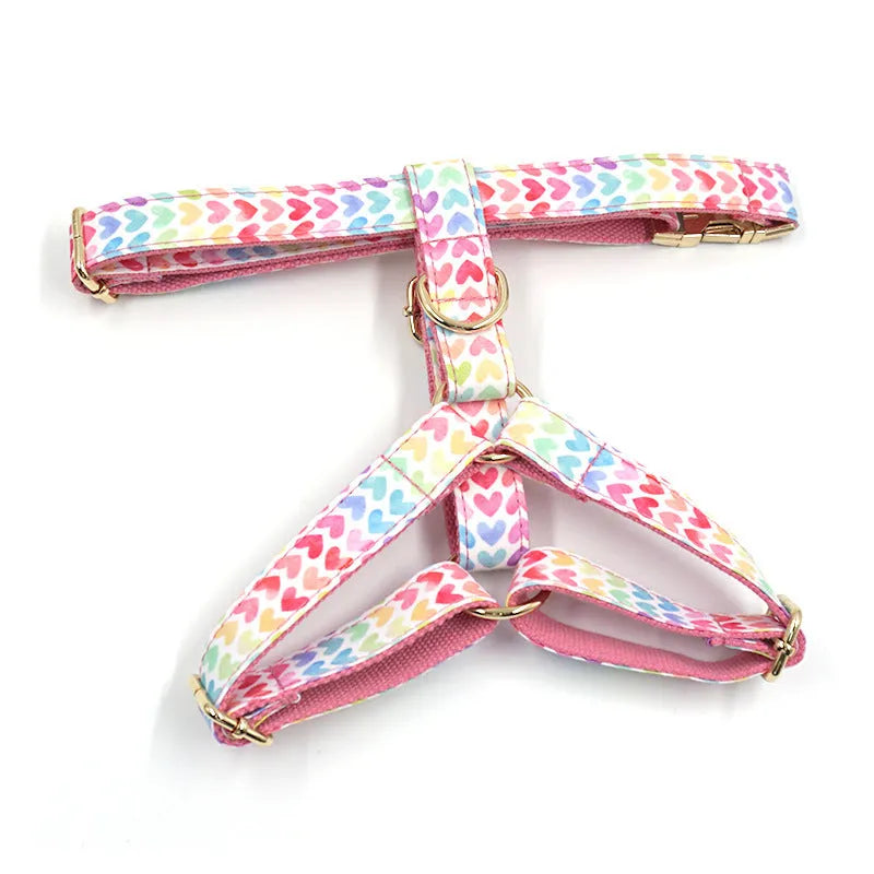 Pink colourful dog harness with gold buckle and heart-shaped stone decoration on a white background.