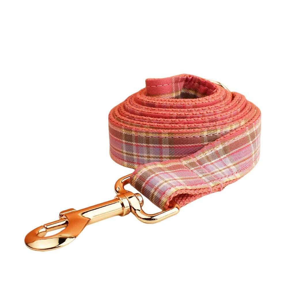 Plaid cloth fabric dog collar, vest, bow tie, and leash set laid out flat.