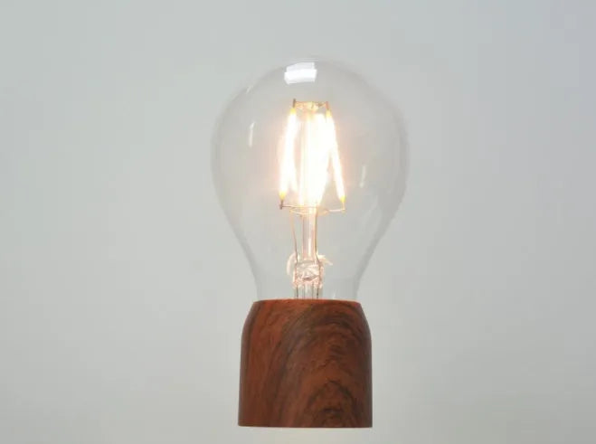 Magnetic levitating light bulb floating above an imitation wood base on a desk.