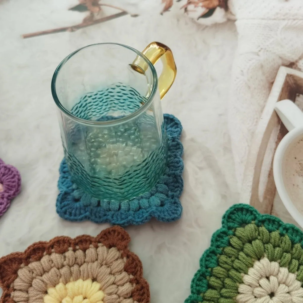 Handmade crocheted wool cup placemat with a grandmother lattice design on a wooden table.