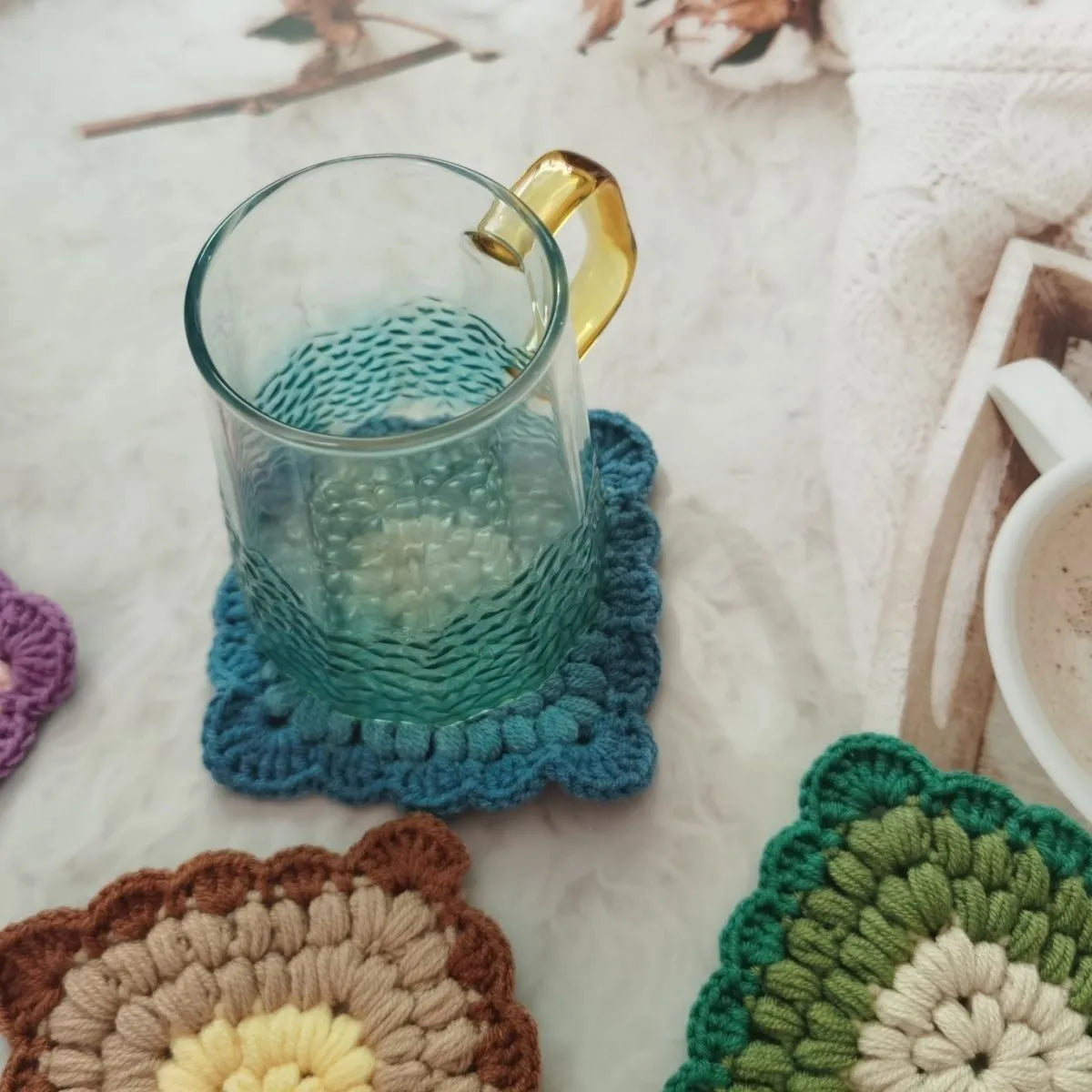 Handmade crocheted wool cup placemat with a grandmother lattice design on a wooden table.