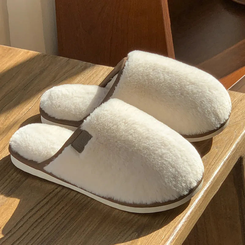 A pair of solid colour winter plush slippers with a PVC sole on a wooden floor.