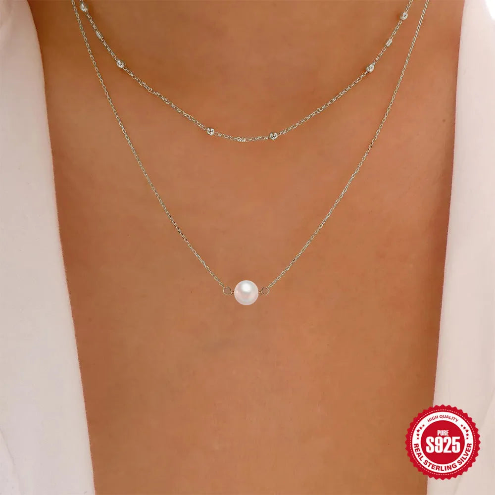 Close-up of a women's double layer sterling silver necklace with two round freshwater pearls on a geometric pendant.