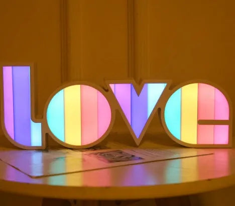 Rainbow-style plastic LED decorative light spelling LOVE, shown on a table.