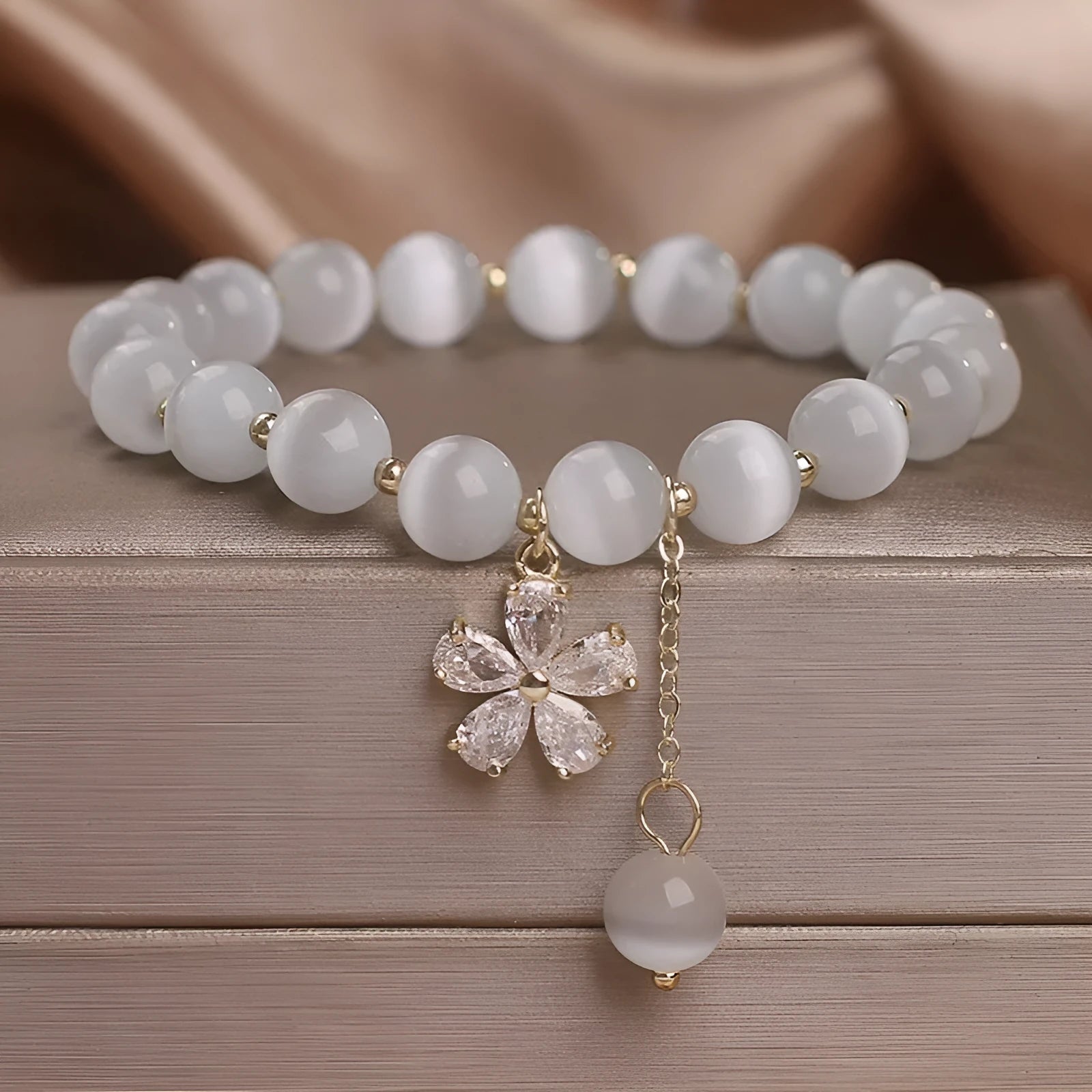 White cat's eye stone bracelet with flower tassel detailing and safety buckle closure