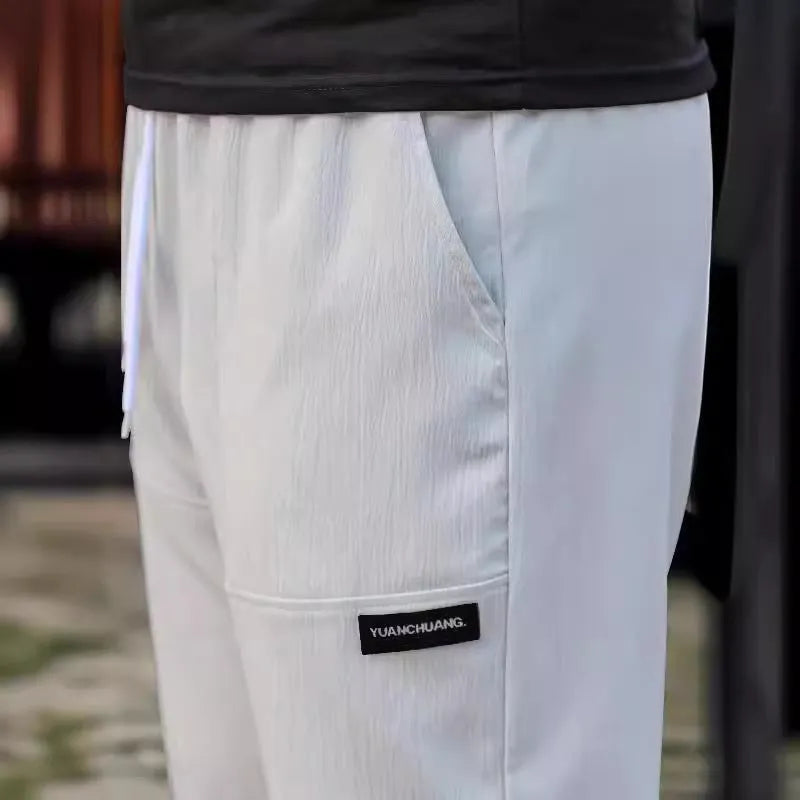 Men's light grey polyester trousers for spring and autumn wear, laid flat.
