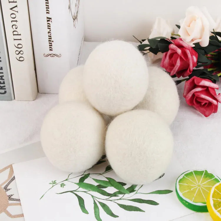 A natural wool drying ball for tumble dryers next to a plain cotton storage bag on a laundry background.