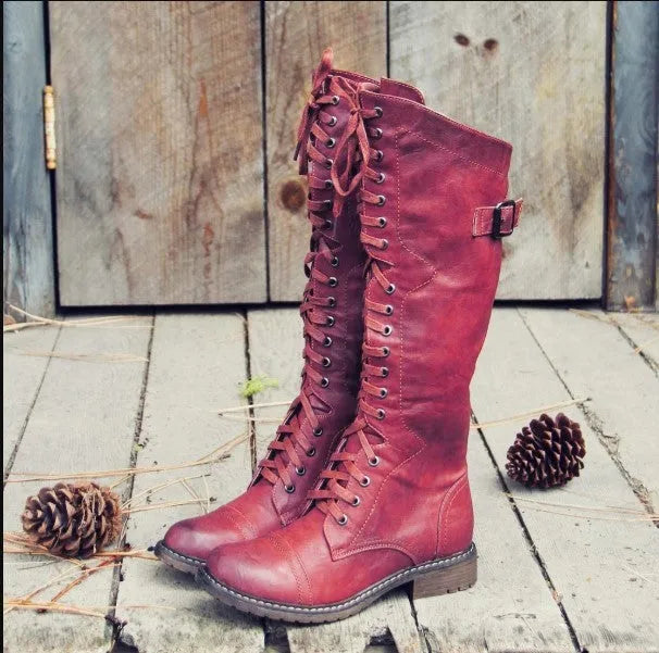 Women's black knee-high boots with a cross-strap buckle and elastic back panel.