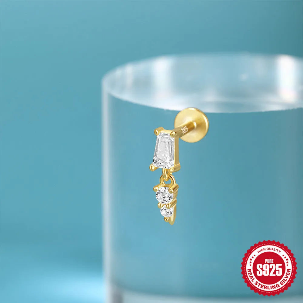 A gold tone sterling silver ear stud featuring a dangling tassel and XINGX inlaid design on the stud.