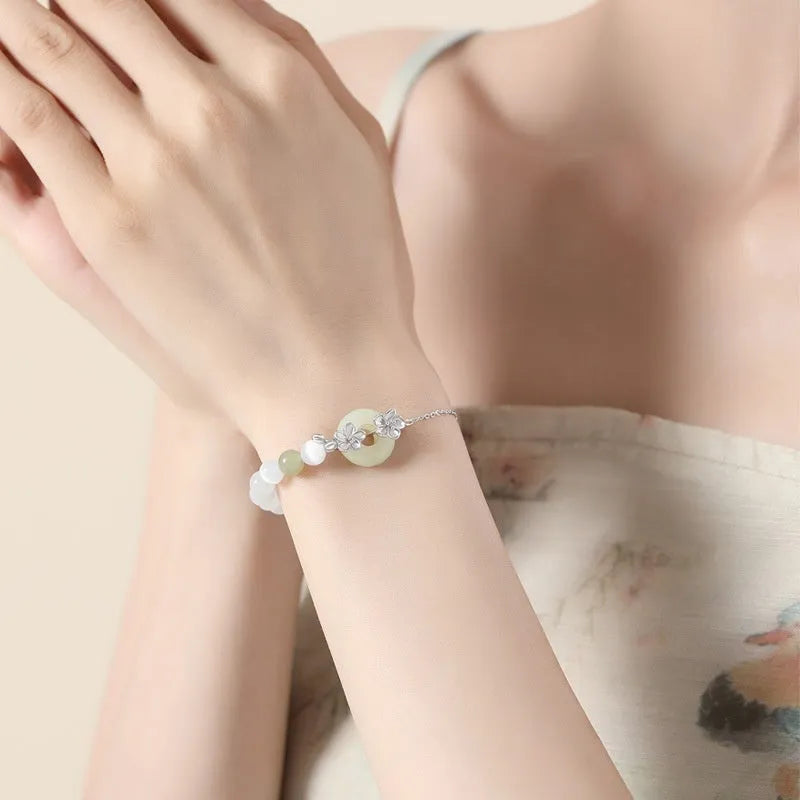 Women's pure silver bracelet with a safety buckle and a peach blossom flower charm in a choice of gold colours.