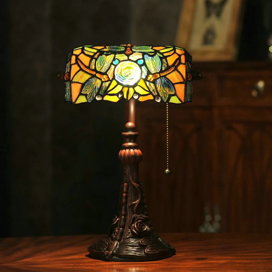 Tiffany style desk lamp with coloured stained glass shade and resin base on a wooden table.