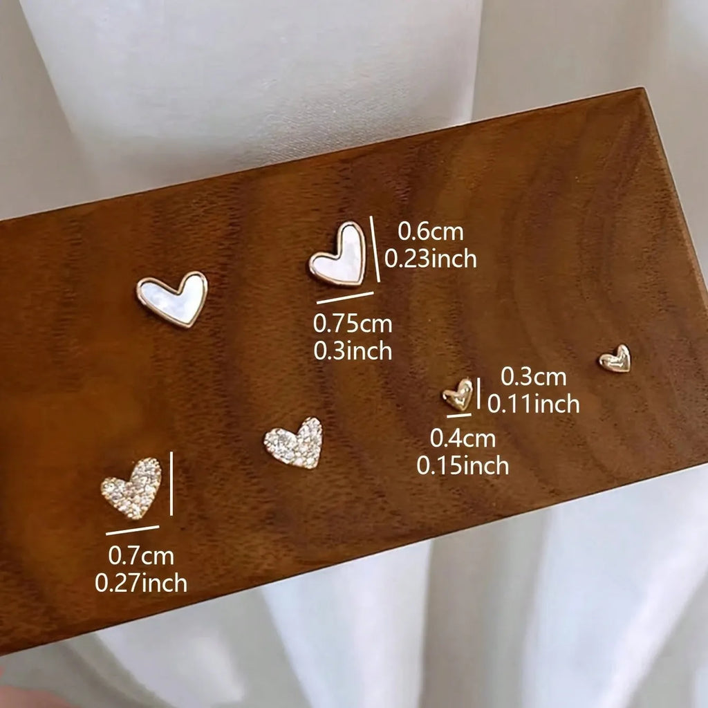Three pairs of women's heart-shaped earrings in gold, black, black and white, and pink colours
