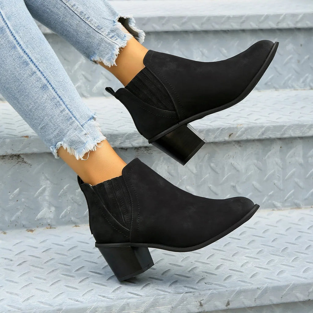 Women's black pointed toe ankle boots with thick square low heel on wooden floor