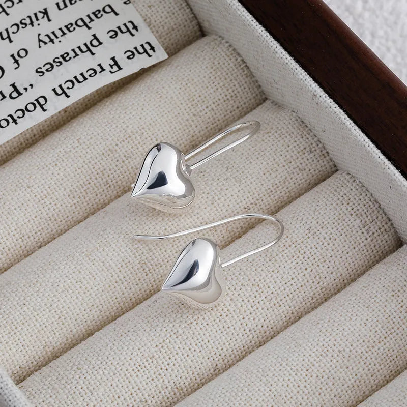 Silver-coloured three-dimensional heart-shaped earrings with glossy finish on copper