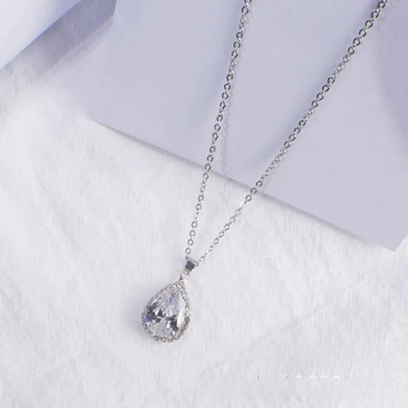 Close-up of a women's rose gold tone drop pendant necklace with pink rhinestone inlay on a model.