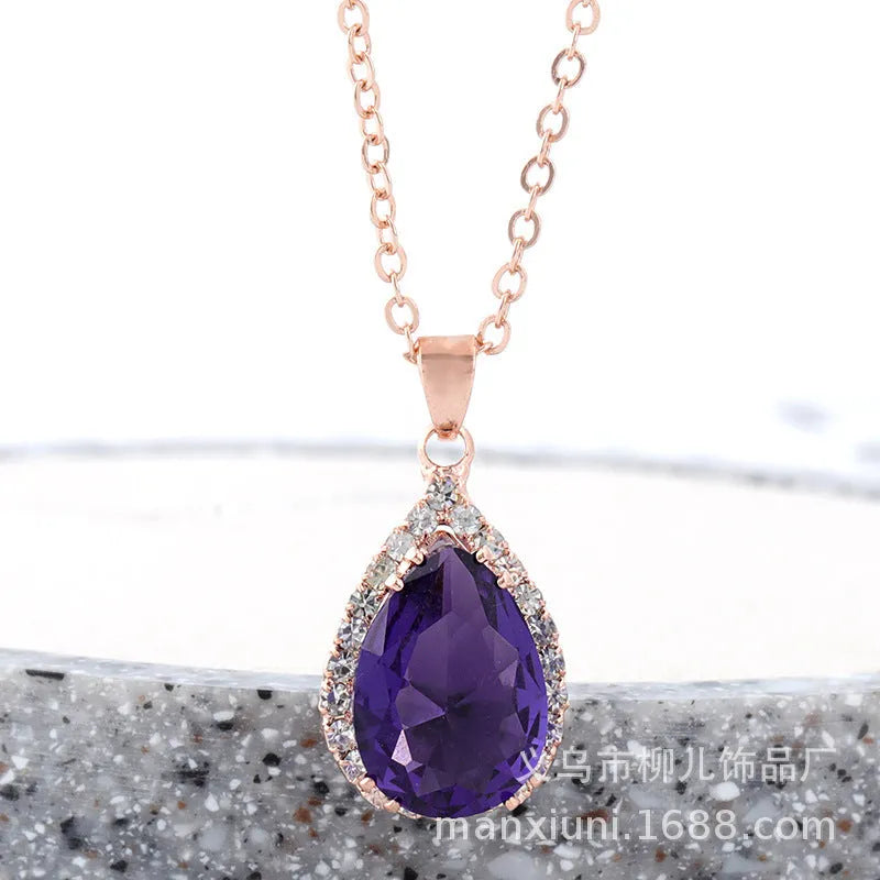 Close-up of a women's rose gold tone drop pendant necklace with pink rhinestone inlay on a model.