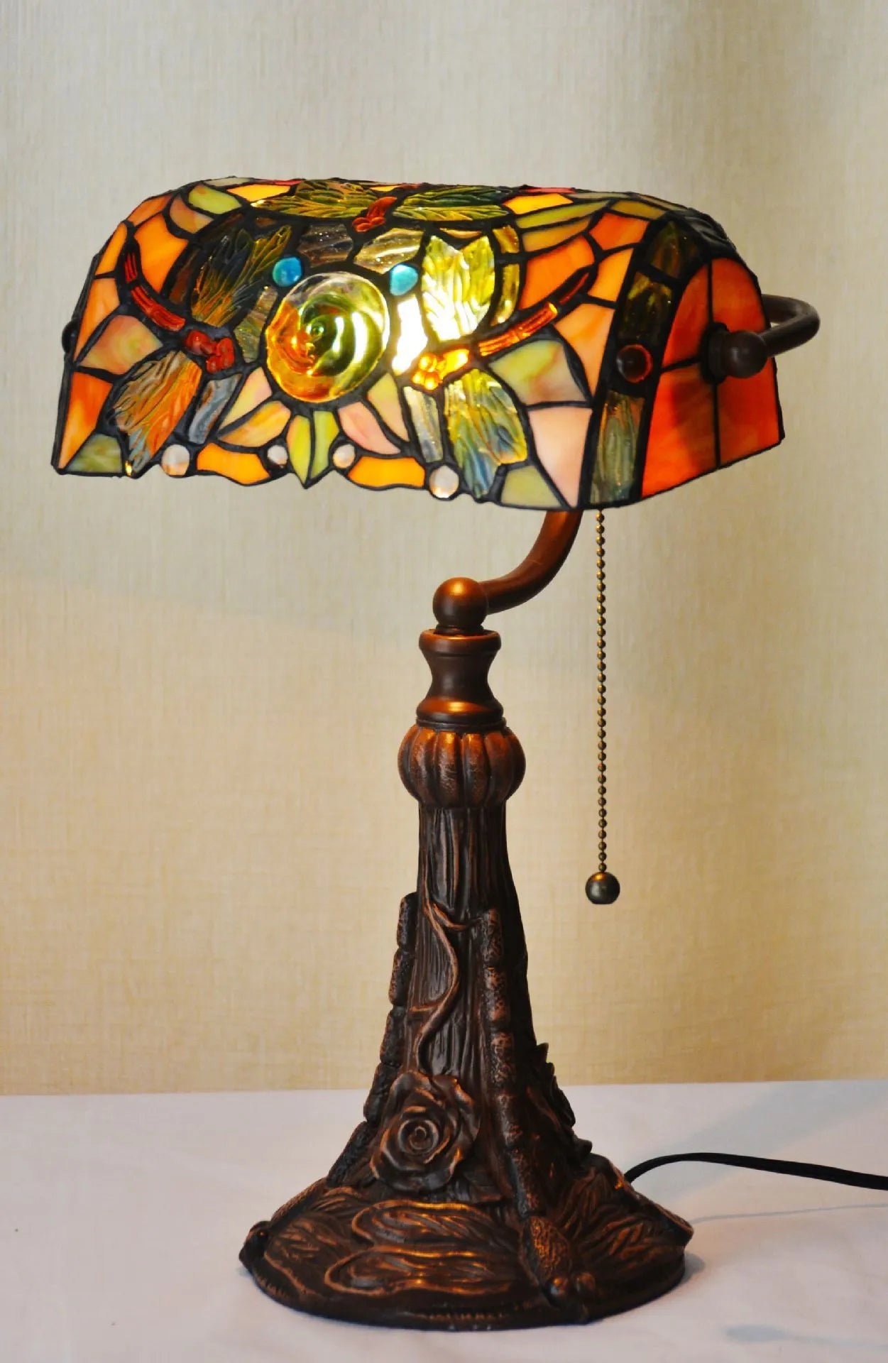 Tiffany style desk lamp with coloured stained glass shade and resin base on a wooden table.