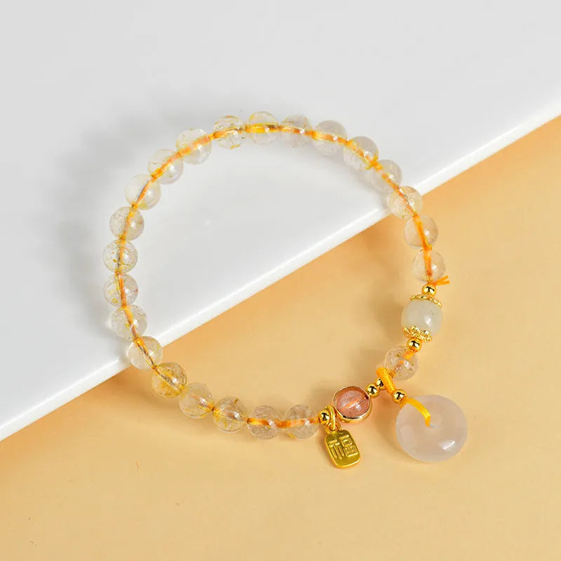 Gold rutilated quartz bracelet with geometric safety buckle and pendant on a white background.