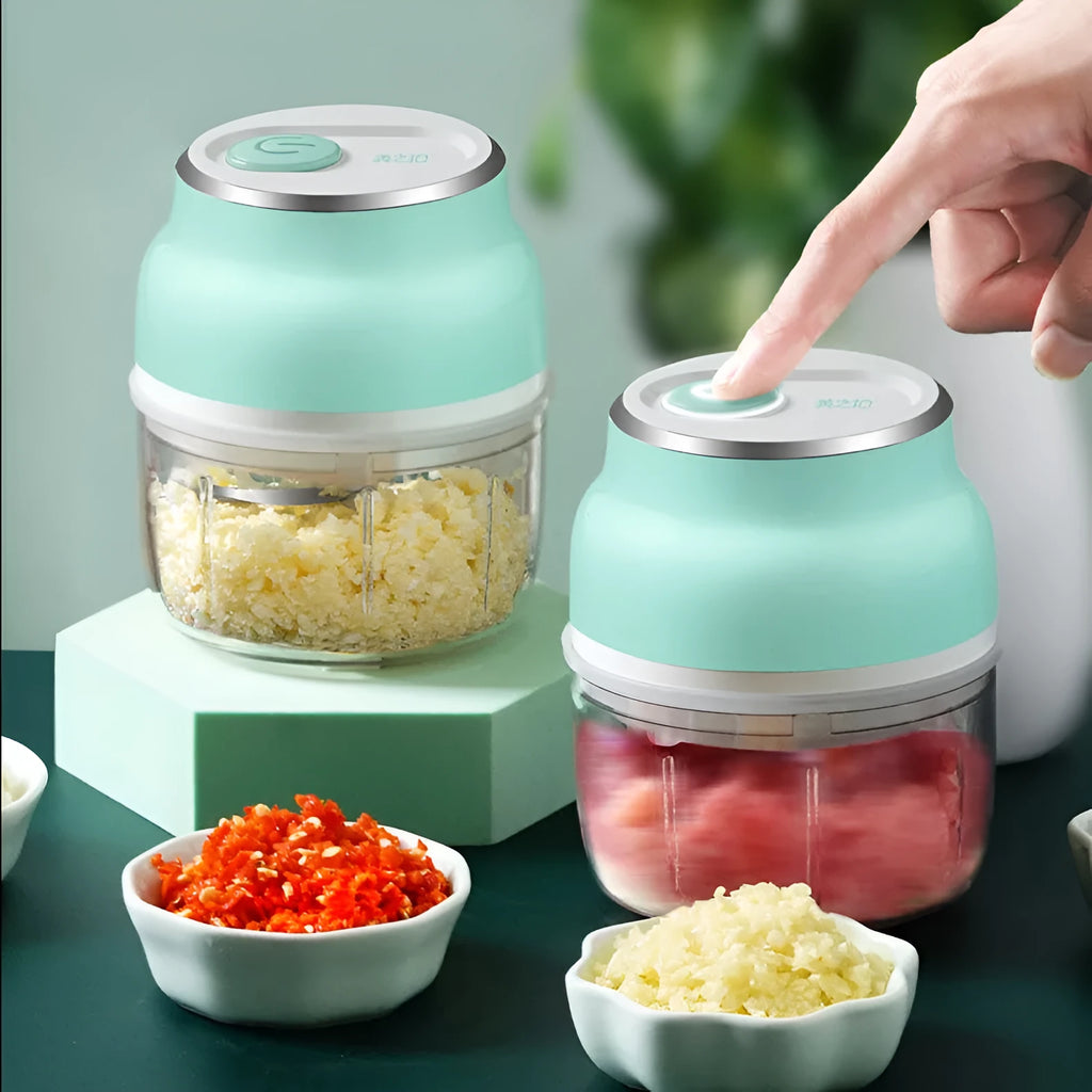 Mini electric food chopper with transparent cup and stainless steel blade on a kitchen counter.
