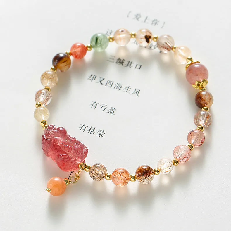 Copper women's bracelet with a pink Strawberry Quartz crystal and a gold-toned Pixiu charm, alongside smaller crystal beads.